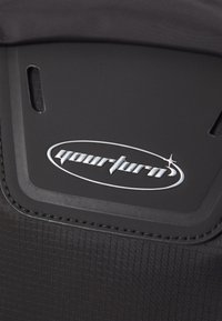 Mochila de tela negra con una textura suave, logotipo prominente de "yourturn" y costuras reforzadas a lo largo de los bordes.