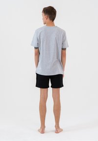 Szara bawełniana koszulka z krótkim rękawem i luźnym krojem, zestawiona z czarnymi bawełnianymi szortami. Tło jest gładkie, białe.