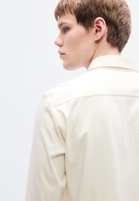 Κρεμ πουκάμισο με κοντά μανίκια και απαλή υφή, με κλασικό γιακά και καθαρό, μίνιμαλ σχέδιο.