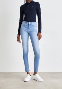 Marineblaues Langarm-Polohemd mit Knöpfen, hellblaue enge Jeans und weiße Sneakers. Einfaches Design, glatte Textur, körpernahe Silhouette.