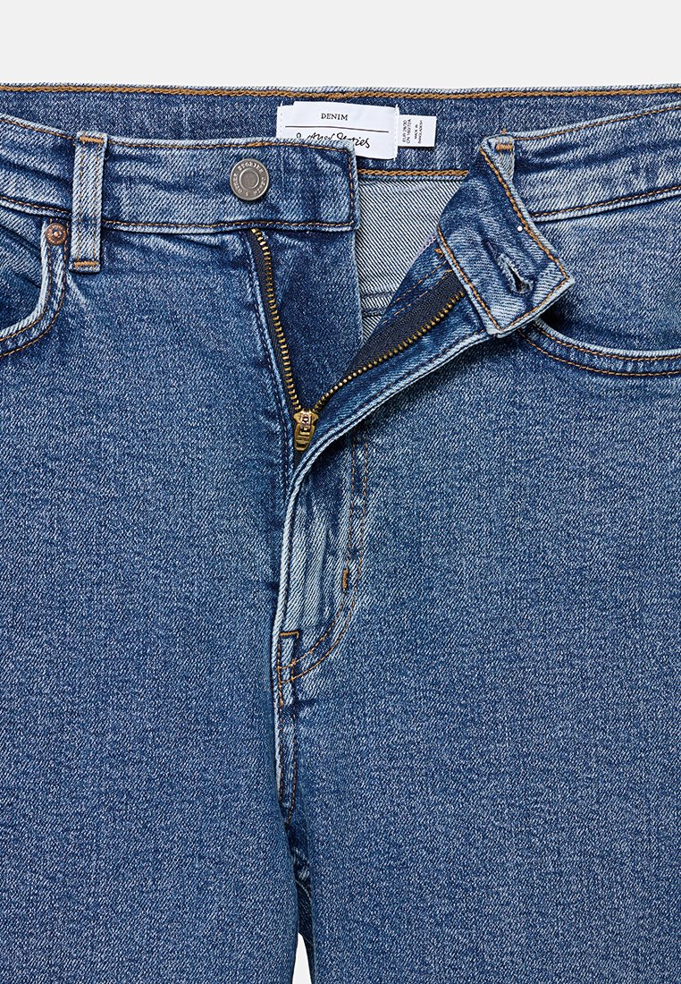 Helle blaue Denim-Jeans mit einem Reißverschluss, Kupferknopfverschluss und standardmäßigem Fünf-Taschen-Design mit sichtbaren Stichdetails.