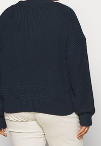 Granatowy, oversize'owy, dziergany sweter z fakturowanym wzorem, prążkowanymi mankietami i spodem. Widok z tyłu ukazuje luźną sylwetkę i bezszwowe wykończenie.