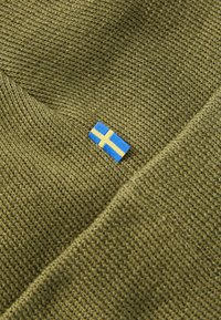 Close-up de tecido de malha verde-oliva com uma pequena etiqueta da bandeira sueca em azul e amarelo cosida.