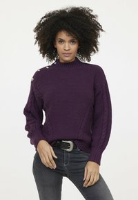 Pull en maille violet avec un col montant, motif texturé, accents en torsades sur les manches et boutons dorés sur l'épaule.