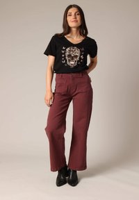 T-shirt noir à col en V avec un graphique de crâne floral, associé à un pantalon bordeaux taille haute, doté de deux poches avant et d'une coupe droite.