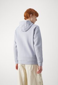 Felpa grigia chiara con cappuccio regolabile, polsini e orlo a coste. Tessuto liscio senza motivi, abbinata a pantaloni cargo crema.