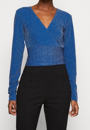 Blauw top met lange mouwen en een diepe V-hals, gemaakt van een textuurrijke, glinsterende stof. Gecombineerd met zwarte, hooggetailleerde broek voor contrast.