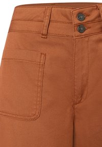 rostfarbene Jeans mit glatter Textur, hohem Bund, zwei Knopfverschlüssen und einer einzelnen Gesäßtasche.