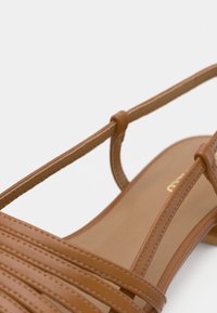 Sandale en cuir marron avec fines brides et petit talon sur fond blanc.