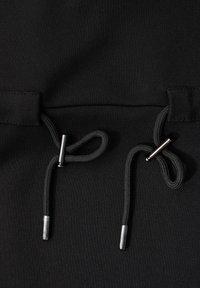 Svart tyg med en slät textur har justerbara dragsnören med metallspetsar, integrerade i plaggets design.