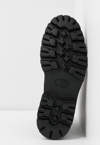 Czarna gumowa podeszwa z głębokim bieżnikiem i teksturowaną powierzchnią. Charakteryzuje się wyrazistymi wzorami i centralnym logo. Płaska, solidna konstrukcja zapewnia przyczepność.