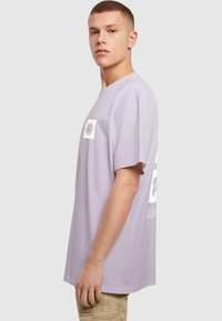 Lys lilla bomuld t-shirt med korte ærmer, med et hvidt grafik på fronten og bagsiden. Casual pasform med en glat tekstur.