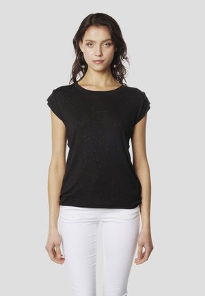 Črna majica s kratkimi rokavi, sproščenega kroja, z nežno bleščečo teksturo. Kombinirana z belimi oprijetimi kavbojkami.