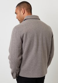 Szara kurtka z mieszanki wełny z ko�łnierzem, o strukturalnym wzornictwie i miękkiej fakturze, widziana z tyłu. Widoczne czarne spodnie.