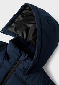Chaqueta acolchada de color azul marino con collar y capucha adjunta, que presenta un forro interno negro brillante y un cierre frontal con cremallera, exhibiendo un material texturizado.