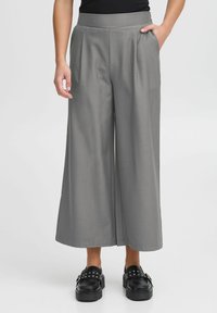 Grijze wijde broek met hoge taille en plooidetails, gecombineerd met zwarte plateau-schoenen met zilveren studs.