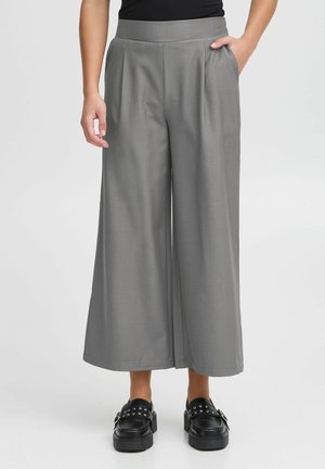 Grijze wijde broek met hoge taille en plooidetails, gecombineerd met zwarte plateau-schoenen met zilveren studs.