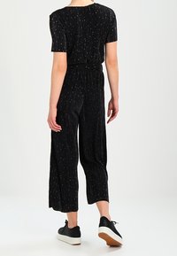 Svart jumpsuit med korta ärmar, vertikala ränder, cinchad midja och vida, korta ben. Bärs med svarta sneakers med vita sulor.