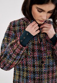 Cappotto in tweed multicolore con un motivo a patchwork di rosso, blu, giallo e nero. Presenta un colletto alto e bottoni frontali.