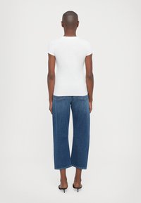 Hvit tettsittende t-skjorte med korte ermer, kombinert med vide blå denimjeans. Glatt tekstur, minimalistisk design, avslappet stil.