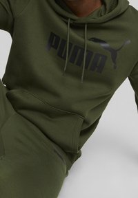 Olivgrön hoodie med känguruficka, som har en stor svart "PUMA"-logga och en hoppande katt-silhuett på bröstet.