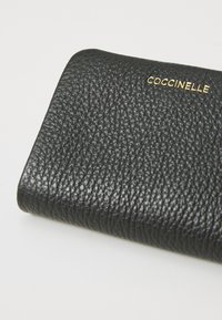 Portafoglio in pelle nera Coccinelle, con superficie testurizzata, forma compatta e dettaglio del logo dorato per un contrasto.