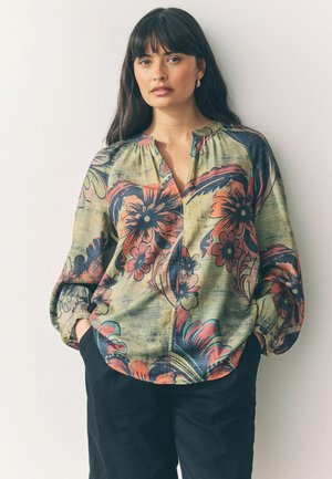 Blusa floreale dallo stile morbido, con una base verde, fiori arancioni e blu brillanti e una scollatura a oblò. Maniche lunghe a sbuffo.
