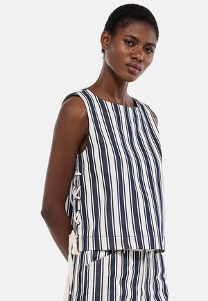 Femme portant un haut sans manches à rayures verticales bleu marine et blanches avec un détail de laçage sur le côté, assorti à un bas à rayures assorties.