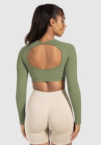 Olijfgroen cropped langarm shirt met een ruguitsnijding, gemaakt van zachte stof. Gecombineerd met lichtbeige hoge taille short.