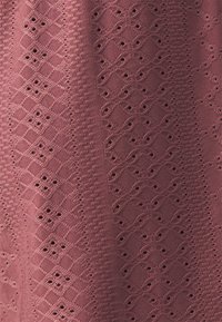Burgundská látka s texturovaným designem, který obsahuje diamantové a vlnité vzory, spolu s malými detaily kolem očí.