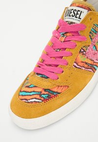 Baskets en suede jaune avec une tige en tissu à motifs orange, turquoise et rose. Présente des lacets roses et une semelle en caoutchouc blanche.