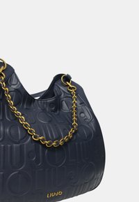 Borsa in pelle blu con design a logo impresso, accentuata da una catena dorata e dalla forma morbida e arrotondata. Presenta un manico superiore e una superficie testurizzata.