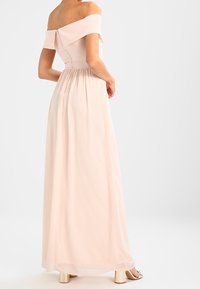 Robe longue à épaules dénudées en tissu rose doux, avec un corsage ajusté, une jupe froncée et un détail subtil dans le dos. Design texturé et fluide.