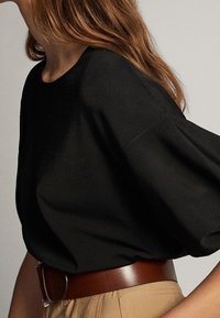 Zwarte gebreide top met een ronde halslijn en korte, brede mouwen. Draagt met een bruine leren riem over beige hoge taille broek.