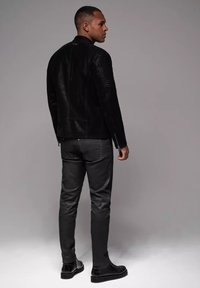 Chaqueta de cuero negra con acentos acanalados en los hombros, combinada con jeans negros ajustados y botas negras con cordones. Textura suave, corte a medida.