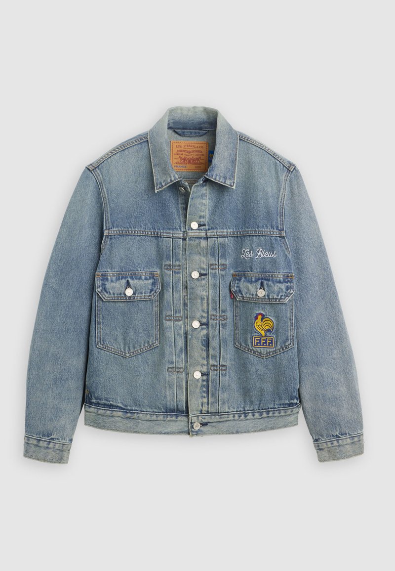 Hellblaue Jeansjacke mit Knopfleiste, zwei Brusttaschen, dem Schriftzug „Les Bleus“ und einem Patch des Französischen Fußballverbands auf der rechten Tasche.