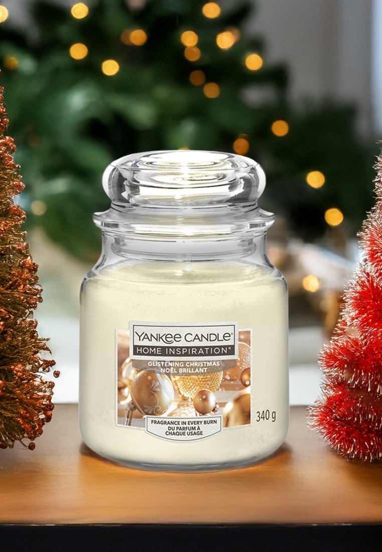 Yankee Candle in un barattolo di vetro trasparente, riempito con cera bianca. L'etichetta presenta dettagli dorati e riporta la scritta "Natale Brillante." 340 g.
