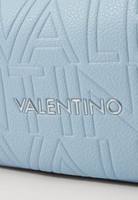 Svetlomodrá kožená taška s vyrazeným logom "VALENTINO", textúrovaným povrchom a jemnými vzorovými detailmi v materiáli.