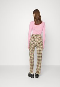 Hose mit einem braunen, grünen und gelben Karomuster. Eng anliegendes Design mit hoher Taille und geraden Beinen, kombiniert mit einem pinken Langarmshirt.