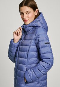 Světle modrá péřová bunda s kapucí, s horizontálními prošívanými pruhy, zipovým zapínáním a logem na levém рукаве.