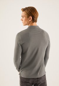 Tricou polo gri cu mâneci lungi dintr-un material moale, cu guler clasic, având o textură netedă și despicături laterale la tiv.