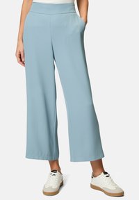 Pantaloni ampi blu chiaro realizzati in morbido tessuto, con tasche laterali e un elastico in vita, abbinati a sneakers bianche e dettagli in marrone chiaro.