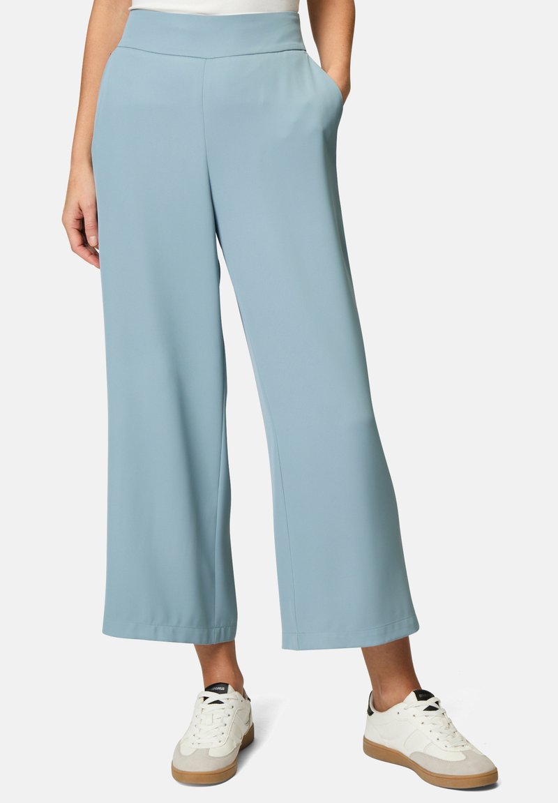 Pantaloni ampi blu chiaro realizzati in morbido tessuto, con tasche laterali e un elastico in vita, abbinati a sneakers bianche e dettagli in marrone chiaro.