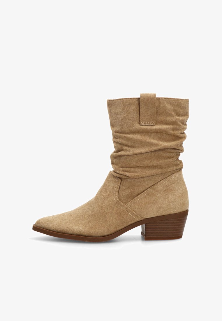 Bota de ante beige hasta la mitad de la pantorrilla con caña arrugada, tira de agarre, puntera afilada y tacón bajo apilado, sobre fondo blanco.