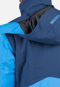 Blau und marineblauer wasserdichter Jacke mit hohem Kragen, Kapuze und schwarzem Innenfutter. Verfügt über ein Logo auf dem Rücken und eine glatte Textur.