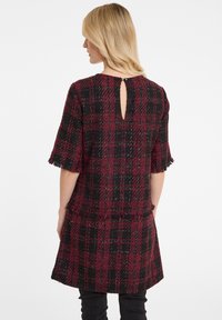 Robe en tweed à motif écossais noir et bourgogne, avec des manches courtes à franges et un détail en trou de serrure au dos. Tissu texturé avec une coupe décontractée.