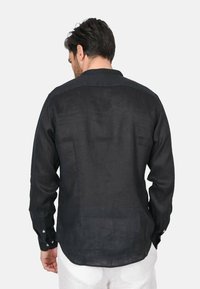 Camicia nera in lino con maniche lunghe, polsini con bottoni, design con yoke sul retro e hem curvo. Il tessuto appare leggermente strutturato e leggero.