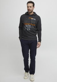 Dark gray hoodie with graphic print in orange and silver, paired with navy pants and white sneakers, featuring a drawstring hood and ribbed cuffs.