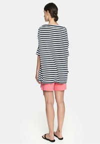 Paskowany, oversize top w granatowym i białym kolorze, w zestawieniu z różowymi szortami. Materiał z mieszanki bawełny, luźny krój i krótkie rękawy.