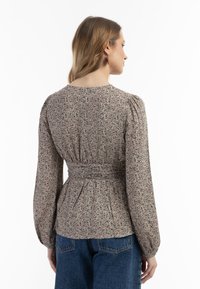 Blus med blommönster som har smal midja, långa puffärmar och rundad halsringning. Tyget har en strukturerad, lätt känsla.